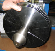 A hand holds a flat metal die that is a custom tooling piece for a Huth bending machine.