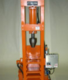 An orange vertical swage press with custom tooling is shown on the floor of a shop.