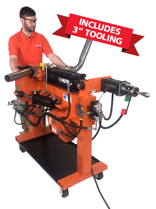 A man in an orange shirt with a beard and safety glasses stands behind the Huth 1605, part of the Huth HB-05 Complete Essentials™ Package. The machine is bright orange with black pipe bender tooling.