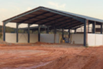 A large open car port structure made with pillars and a tin roof on a dirt road.