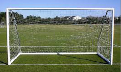 A white soccer goal net stands at the end of a grassy green playing field. The goal is made from bent metal pipe.